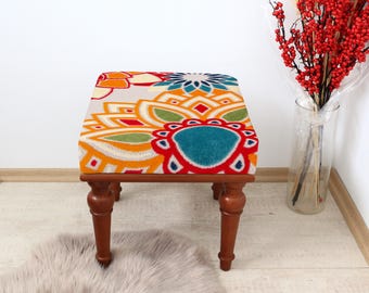 Cómodo taburete con diseño floral colorido, asiento cuadrado tapizado, taburete otomano vintage, detalle decorativo para dormitorio o sala de estar.