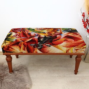 May include: A wooden bench with a colourful abstract design on the seat. The seat features a vibrant mix of red, orange, yellow, green, and black hues. The bench has four turned legs and is placed on a light-coloured floor.