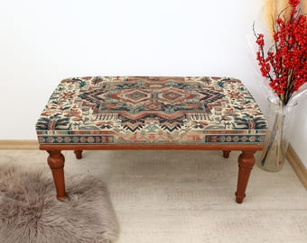 May include: A wooden ottoman with a patterned fabric top. The fabric features a geometric design in shades of red, blue, and green.