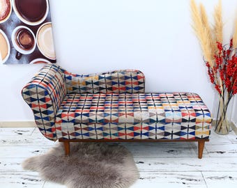 Könnte beinhalten: Eine farbenfrohe, gemusterte Chaiselongue mit Holzbeinen. Die Chaiselongue ist mit einem Stoff mit einem geometrischen Muster in Rot, Blau, Gelb und Weiß bezogen.