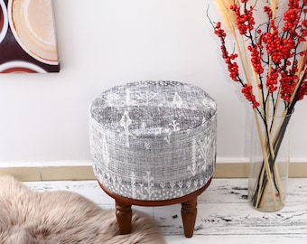 May include: A round grey and white patterned ottoman with wooden legs. The ottoman is sitting on a white floor with a fluffy rug in front of it.