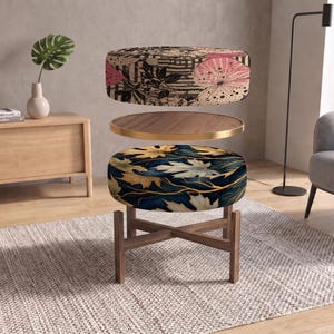 May include: A multi-tiered circular ottoman featuring a top cushion with a beige, black, and pink abstract pattern, a middle wooden tray with a gold rim, and a bottom cushion with a dark blue and gold leaf print on a wooden cross-leg base.