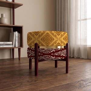 May include: A round ottoman featuring a two-tone design with a gold-colored metal band separating the top and bottom sections. The top is upholstered in yellow fabric with a brown damask pattern, while the bottom has a dark red fabric with a white damask pattern, supported by four dark brown wooden legs.