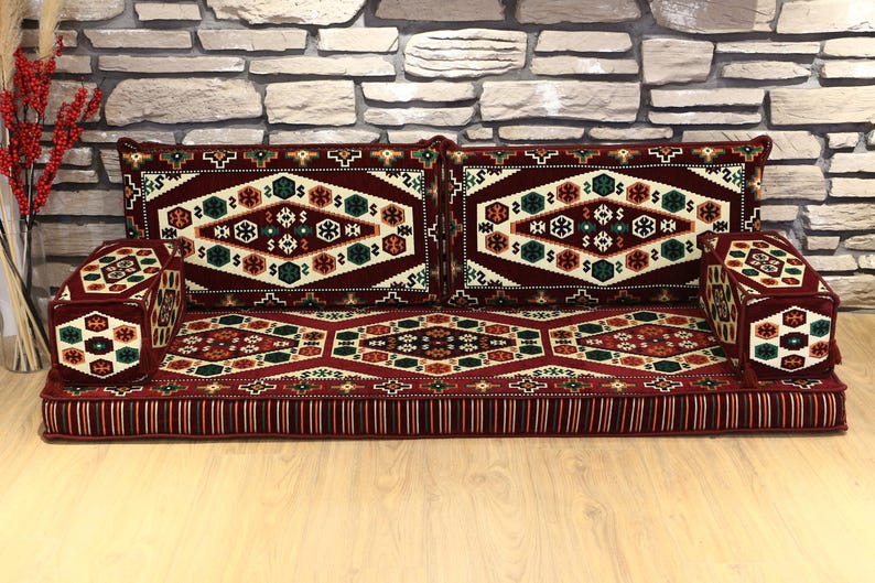 Op de afbeelding: Een vloerzitting met een patroon in tinten bordeauxrood, cr&egrave;me, groen en bruin. De set bevat een lange, rechthoekige basis, twee rugkussens en twee armleuningkussens. De kussens hebben een geometrisch patroon.