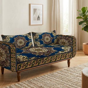 Może przedstawiać: Dwuosobowa sofa tapicerowana głęboką niebieską tkaniną z misternym, wielokolorowym wzorem kwiatowym i medalionami. Mebel posiada prostokątne oparcie, dwie pasujące poduszki i wspiera się na czterech ciemnobrązowych drewnianych nogach.