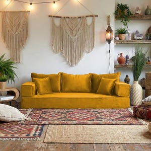 May include: A cozy living room with a mustard yellow sofa, patterned rugs, and macrame wall hangings. The room is filled with plants, including ferns and snake plants, and has a bohemian aesthetic. Decorative pillows and poufs add to the inviting atmosphere.