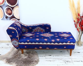 May include: A blue and red patterned chaise lounge with wooden legs. The chaise lounge is upholstered in a fabric with a geometric design.