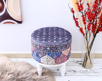 May include: A round, white ottoman with a blue and red patterned fabric top. The ottoman has four white legs and is sitting on a white floor.