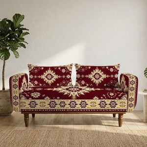 May include: A two-seater sofa featuring a deep red fabric with a cream-colored intricate floral and geometric pattern. The sofa has rounded arms, a straight back, and four short, dark wooden legs. The upholstery covers the seat, back, and arms.
