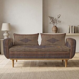 Może przedstawiać: Dwuosobowa sofa wykonana z brązowej i ciemnoszarej tkaniny o splocie, ozdobiona geometrycznym wzorem w romby na poduszkach oparcia oraz powtarzającym się motywem kół wzdłuż podstawy, wsparta na czterech jasnych, zwężających się drewnianych nogach.
