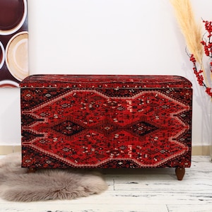 May include: A red and black patterned storage ottoman with a tufted top. The ottoman has a traditional rug design.