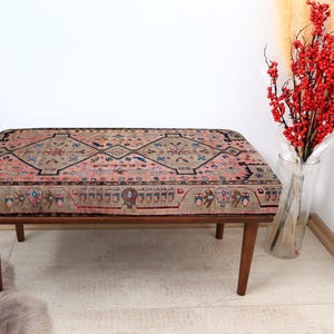 May include: A wooden bench with a colorful patterned cushion. The cushion has a geometric design with shades of pink, blue, and brown.