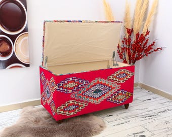 May include: A red storage ottoman with a colorful geometric pattern and a beige fabric lining. The lid is open, revealing the interior of the ottoman.