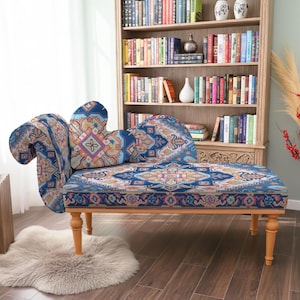 May include: A blue upholstered chaise lounge with a patterned design, wooden legs, and a curved armrest. The chaise is placed in a room with a bookshelf, a wooden side table, and a faux fur rug.