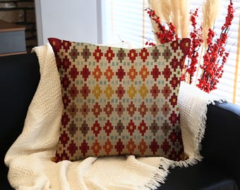 May include: A decorative throw pillow with a geometric pattern in shades of red, orange, yellow, and blue. The pillow is placed on a black sofa and a white blanket. The pillow's design features a repeating diamond pattern.