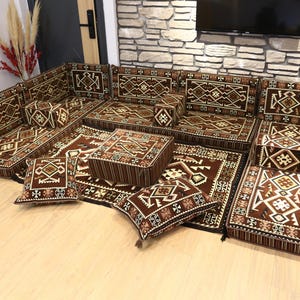 May include: A modular brown sofa set with geometric patterns. The set includes floor cushions, backrests, and square pillows. The design features a mix of brown, beige, and white colors, creating a warm and inviting aesthetic. The set is arranged on a light-colored wooden floor.