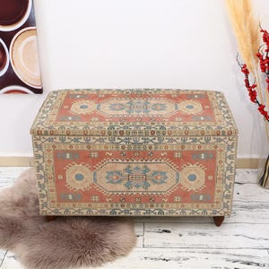 May include: A rectangular storage ottoman with a colorful patterned fabric top. The fabric features a traditional design with red, blue, and cream colors.