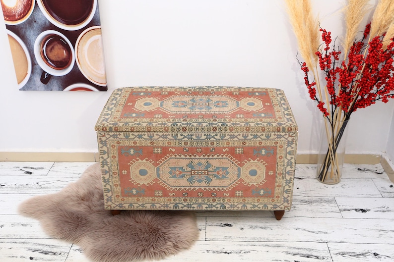 May include: A rectangular storage ottoman with a colorful patterned fabric top. The fabric features a traditional design with red, blue, and cream colors.