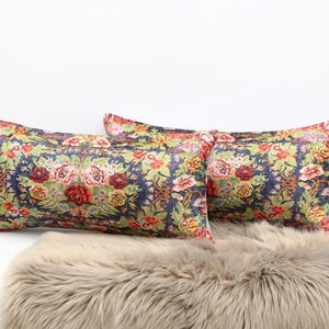 May include: Two decorative throw pillows with a floral pattern on a blue background. The pillows are on a light brown faux fur throw.