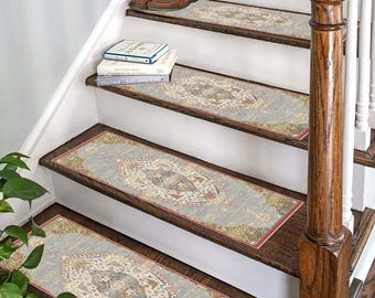 May include: A set of four blue and beige patterned stair treads with a red border. The treads are placed on a wooden staircase with a brown handrail.