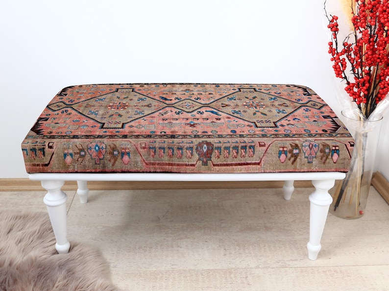 May include: A white wooden bench with a pink and beige patterned rug top. The rug has a geometric design with intricate details.
