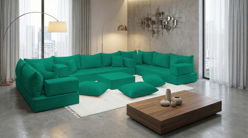 May include: A large, modular emerald green sectional sofa with multiple cushions and ottomans. The sofa is arranged in an L-shape, with a matching square ottoman and several throw pillows. A wooden coffee table and decorative vases are in front.