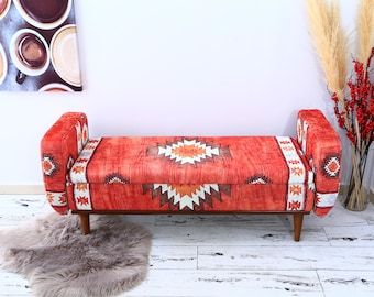 Könnte beinhalten: Eine rote und weiße gemusterte Aufbewahrungsbank mit Holzbeinen. Die Bank hat ein geometrisches Design und ist perfekt, um jedem Raum einen Hauch von Stil zu verleihen.