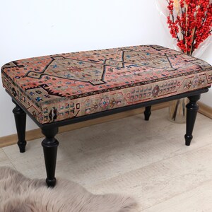 May include: A black wooden bench with a colorful patterned cushion. The cushion has a pink, beige, and blue floral design. The bench has turned legs and is sitting on a light wood floor.