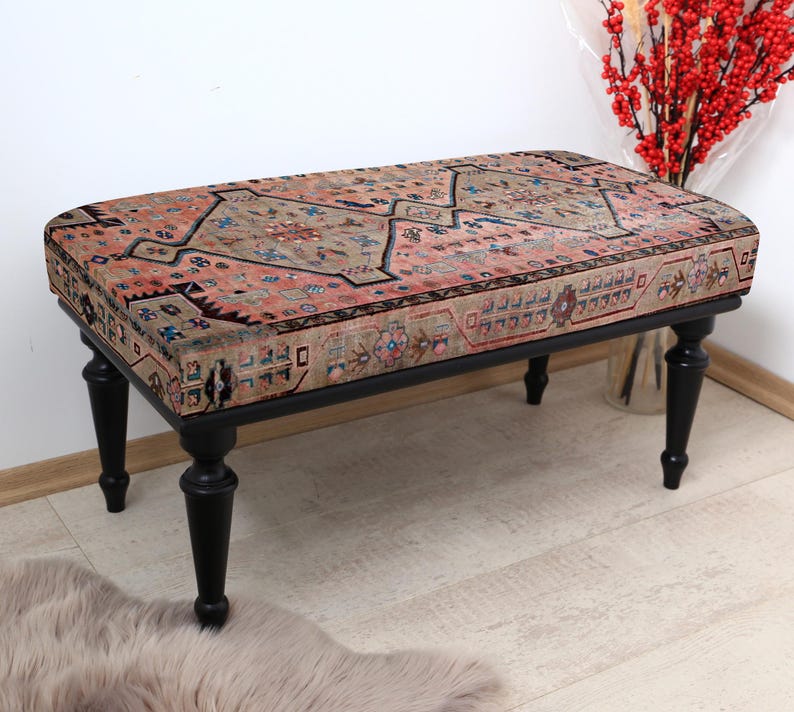 May include: A black wooden bench with a colorful patterned cushion. The cushion has a pink, beige, and blue floral design. The bench has turned legs and is sitting on a light wood floor.