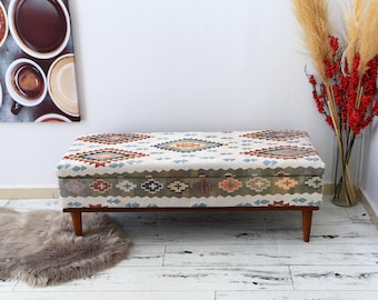 May include: A white storage ottoman with a colorful geometric pattern. The ottoman has a wooden frame and legs.