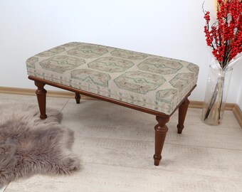 May include: A wooden bench with turned legs and a patterned fabric cushion. The cushion has a geometric design in shades of beige, green, and brown.
