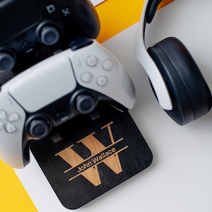 May include: A black wooden stand with a personalised inscription "John Wallace" and a large wooden letter "W" for holding two video game controllers and a pair of white headphones.