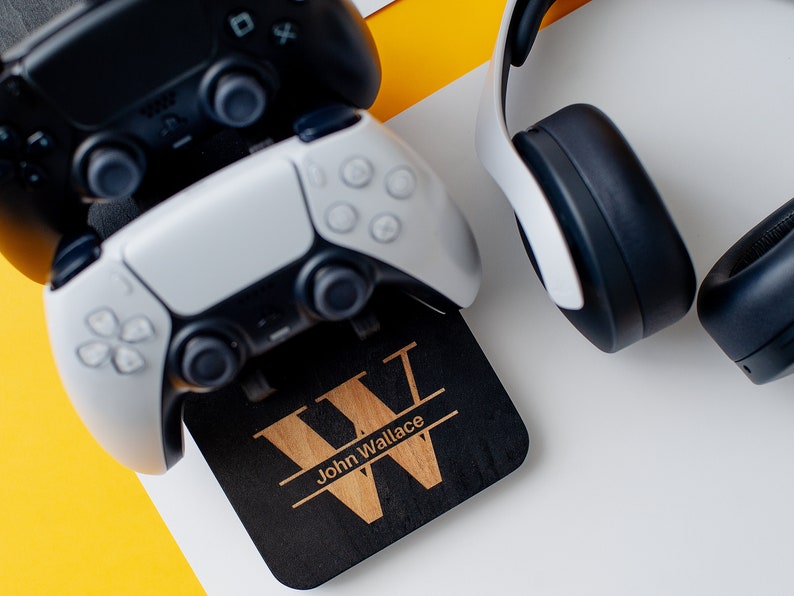 May include: A black wooden stand with a personalised inscription "John Wallace" and a large wooden letter "W" for holding two video game controllers and a pair of white headphones.