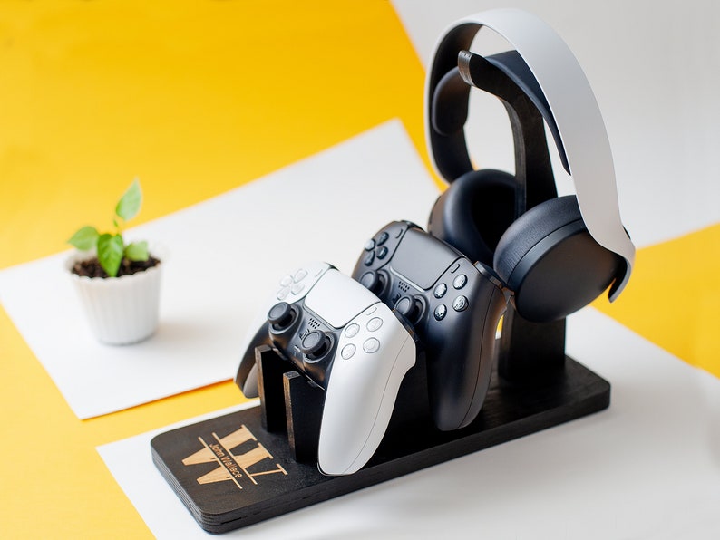 May include: A black wooden stand with a white and black gaming headset, a white and black controller, and a black controller. The stand has the text "III" engraved on it.