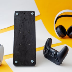May include: A black wooden stand with four rubber feet, a black wireless controller, and a white wireless headset. The stand is on a yellow surface.