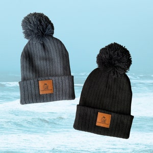 May include: Two black knit beanies with pom poms and a brown leather patch that says "Down South Surf".
