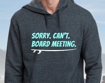 May include: A dark gray hooded sweatshirt with the text "SORRY. CAN'T. BOARD MEETING." in white and a light blue surfboard graphic.