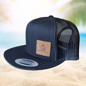 Puede incluir: Gorra de camionero de malla negra y marrón con un parche de cuero que dice "Down South Surf" y una palmera con tablas de surf. La gorra tiene un cierre de presión negro y una pegatina blanca que dice "The Authentic Snapback Tucson Since 1974."