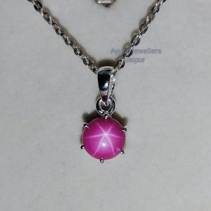Könnte beinhalten: Eine silberne Kettenkette mit einem rosa Stern-Saphir-Anhänger. Der Anhänger ist oval geformt und hat einen sechszackigen Stern in der Mitte.