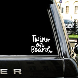 May include: A black car with a white vinyl sticker on the back window that says "Twins on Board."