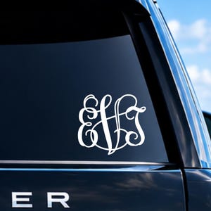 May include: A white vinyl decal featuring a stylized three-letter monogram with the letters E, V, and J in an interlocking cursive script font, applied to the dark tinted rear window of a vehicle.