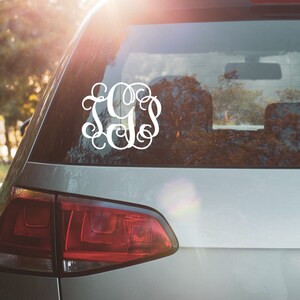 May include: A silver car with a white monogram sticker on the back window. The monogram is a stylized design of the letters "JGS".