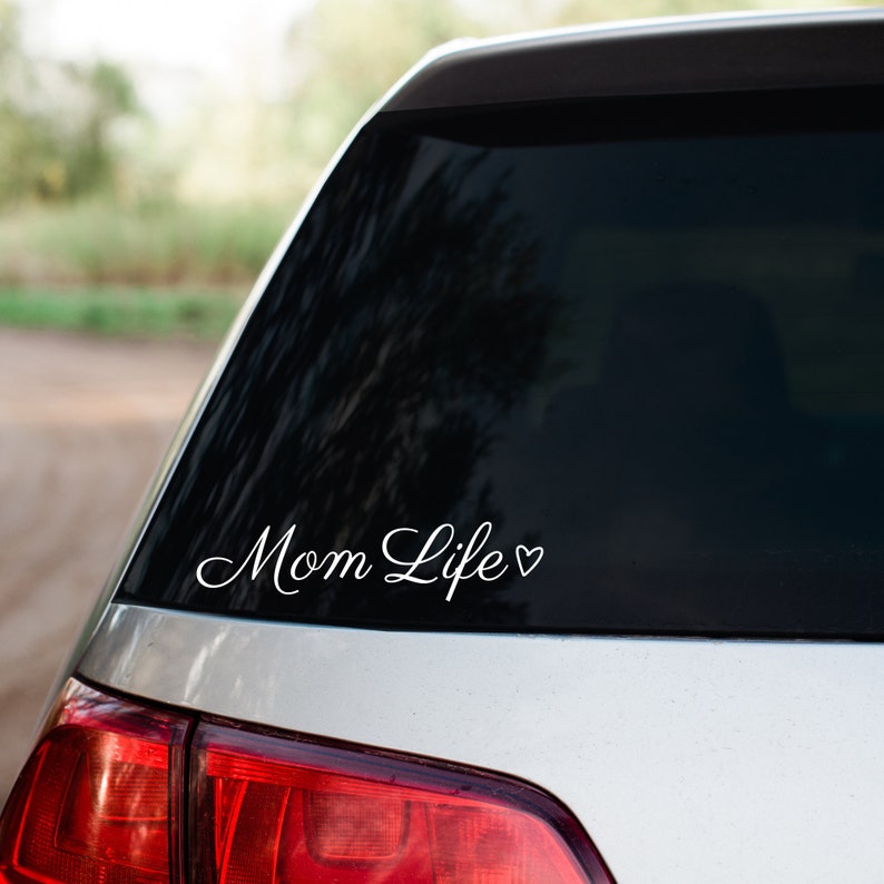May include: White vinyl decal with the text "Mom Life" and a small heart symbol on a silver car.