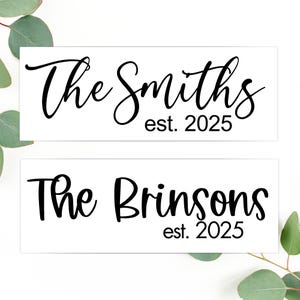 May include: Two white signs with black text. The top sign reads "The Smiths est. 2025". The bottom sign reads "The Brinsons est. 2025".
