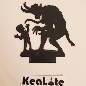 May include: Black silhouette of a devil with horns and a child standing on a base. The devil is reaching out to the child. The base is textured and has a shadow underneath.
