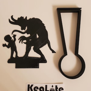 May include: Black silhouette of a devil and a child, with a separate black silhouette of a candle holder. The candle holder is shaped like a tall, thin rectangle with a round base. The text "KeaLite" is printed on a white sticker.