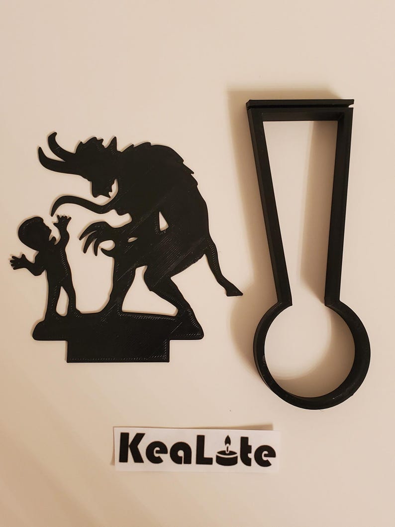 May include: Black silhouette of a devil and a child, with a separate black silhouette of a candle holder. The candle holder is shaped like a tall, thin rectangle with a round base. The text "KeaLite" is printed on a white sticker.