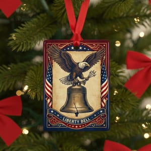 May include: A rectangular ceramic Christmas ornament featuring a bald eagle perched atop a cracked bell. The design includes two American flags, decorative scrollwork, and the text Liberty Bell at the bottom. It hangs from a red satin ribbon.