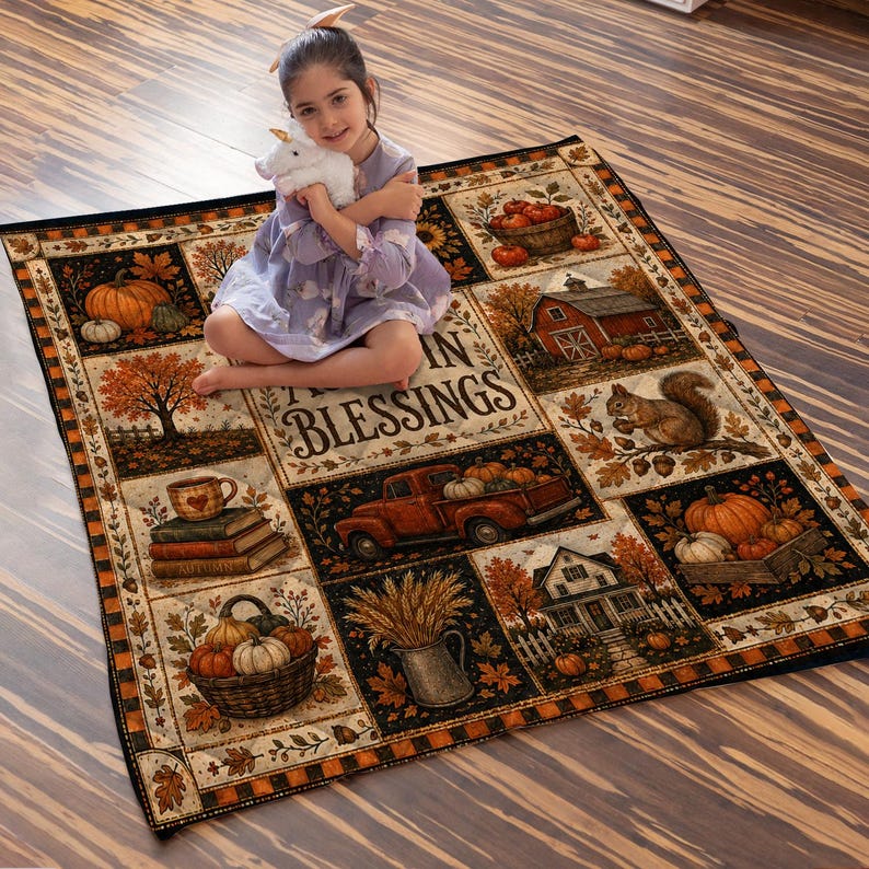 May include: A rectangular throw blanket featuring a patchwork design with autumn-themed illustrations including pumpkins, a red truck, a barn, a squirrel, and a basket of gourds, with the text "AUTUMN BLESSINGS" printed in the center of the blanket.