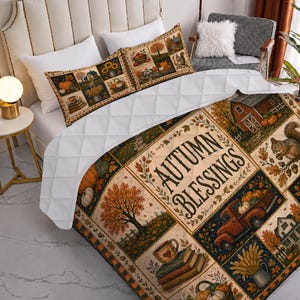 May include: A quilted bedspread and matching pillow shams featuring a patchwork design with autumn-themed illustrations of pumpkins, a red truck, a house, and a squirrel. The central panel displays the text "AUTUMN BLESSINGS" in dark lettering.